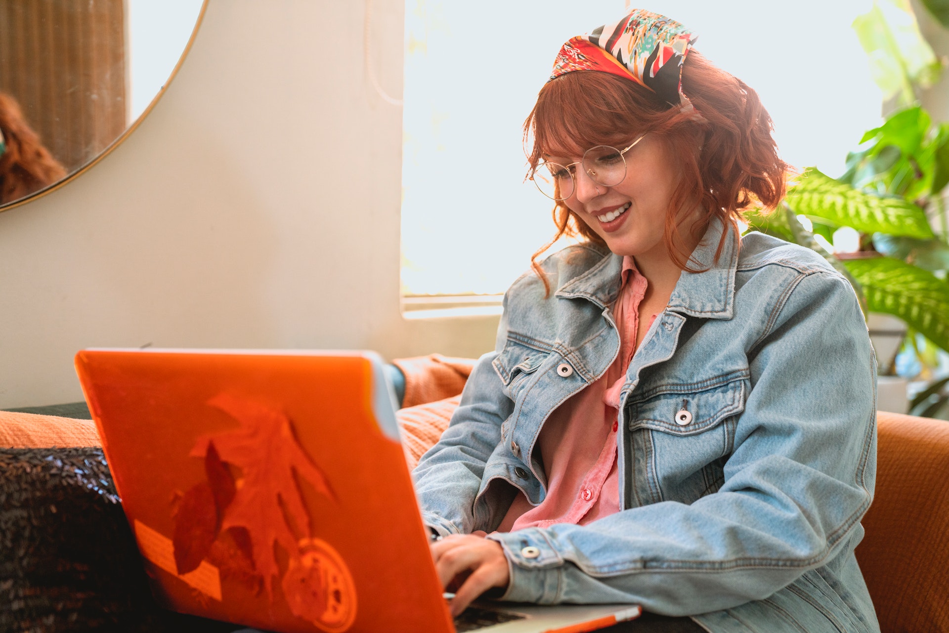 Młoda kobieta w okularach i jesiennych kolorach pisze CV na laptopie siedząc na home office